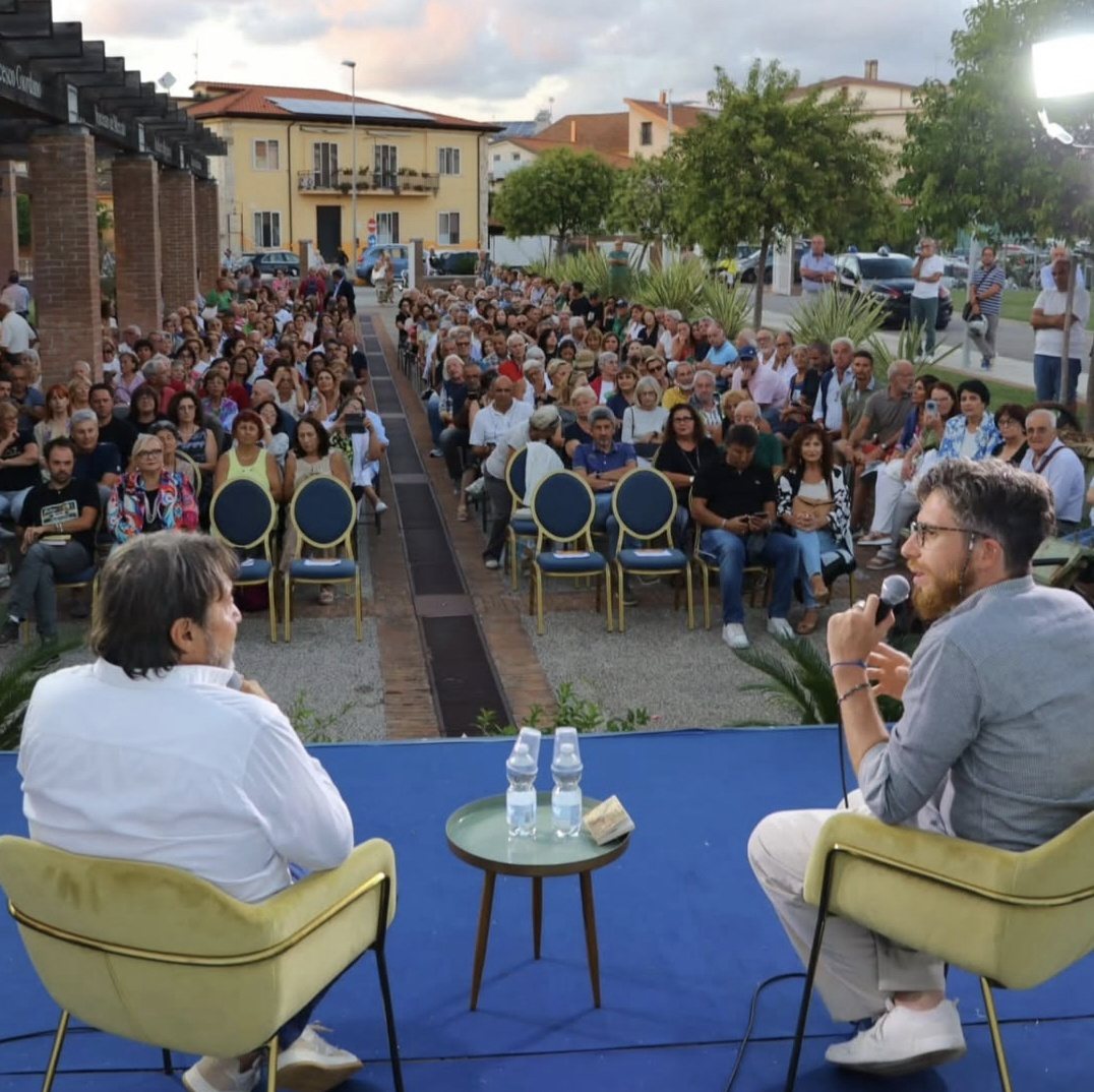 Andrea Parrella modera un incontro all'aperto davanti a un pubblico numeroso