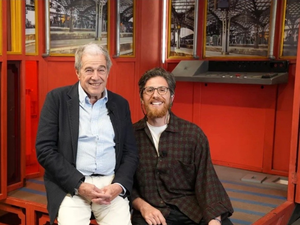 Andrea Parrella seduto accanto a Giovanni Minoli in uno studio dalle pareti rosse